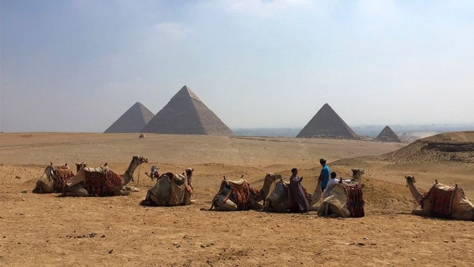 Camels rest between rides with their owners against the backdrop of the pyramids in Giza, Egypt, in 2015. 